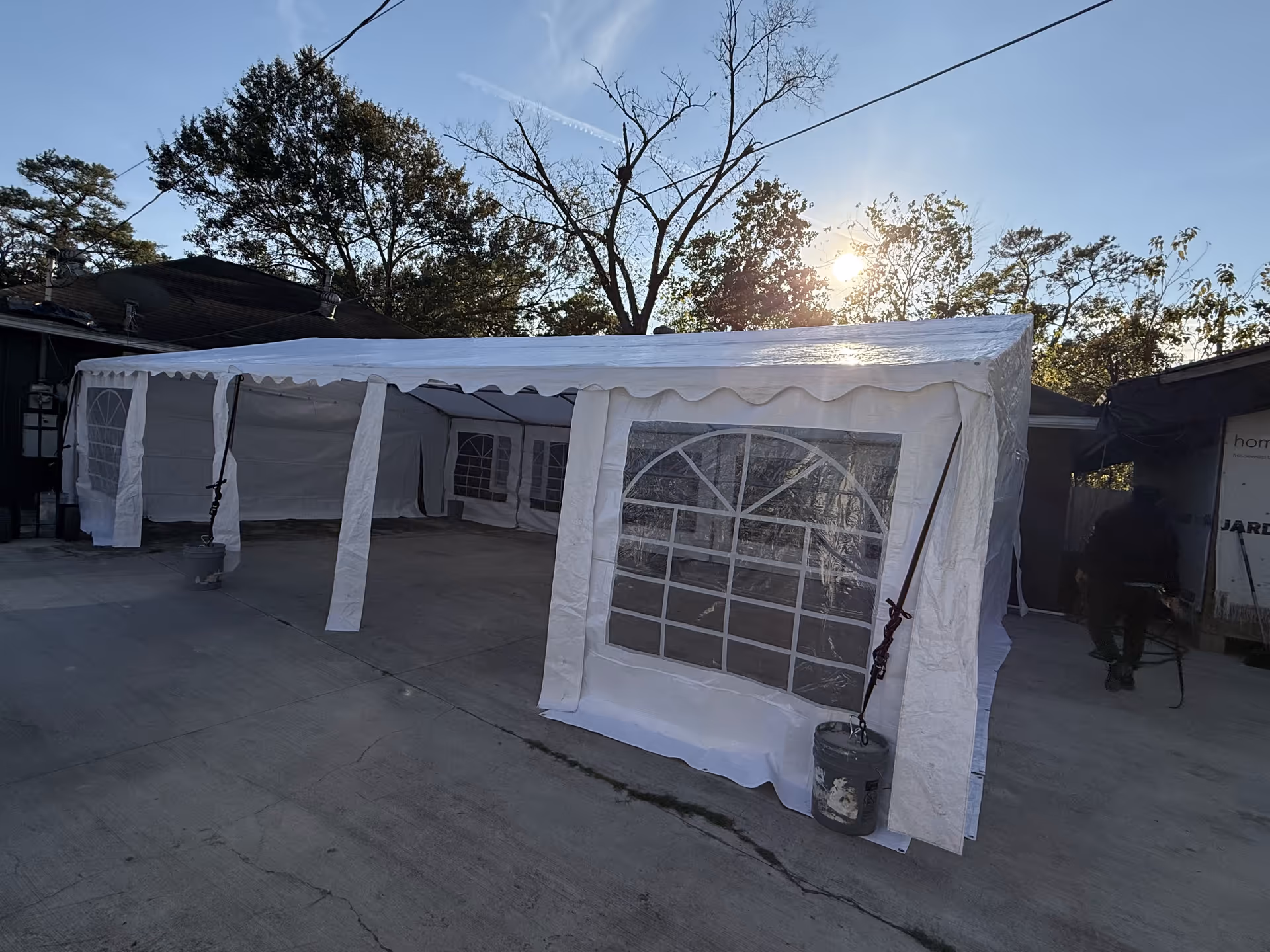 White event tent set up outdoors in a concrete lot beside buildings.