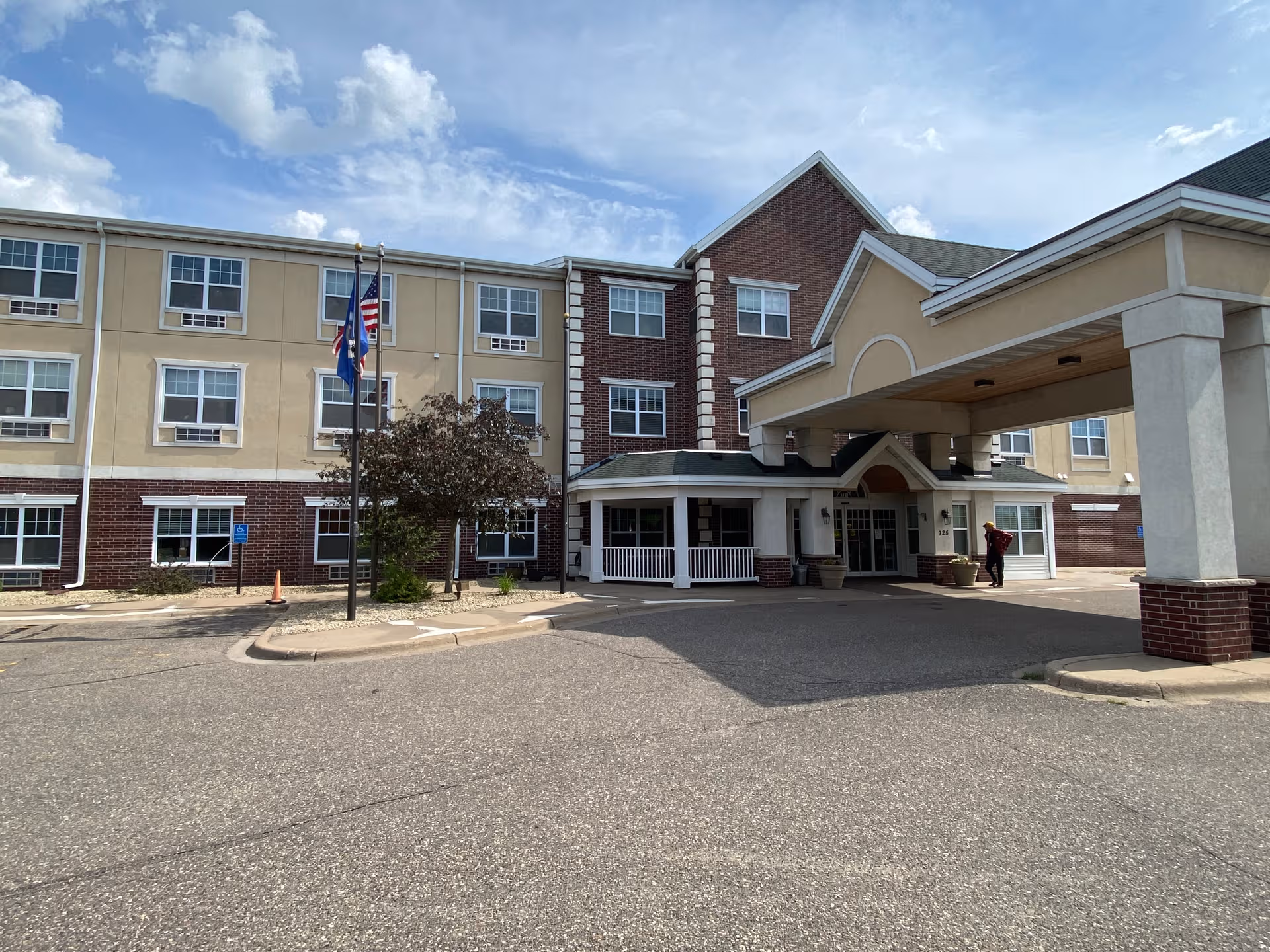 Senior living facility exterior with porte-cochere, flags, and accessible entrance.