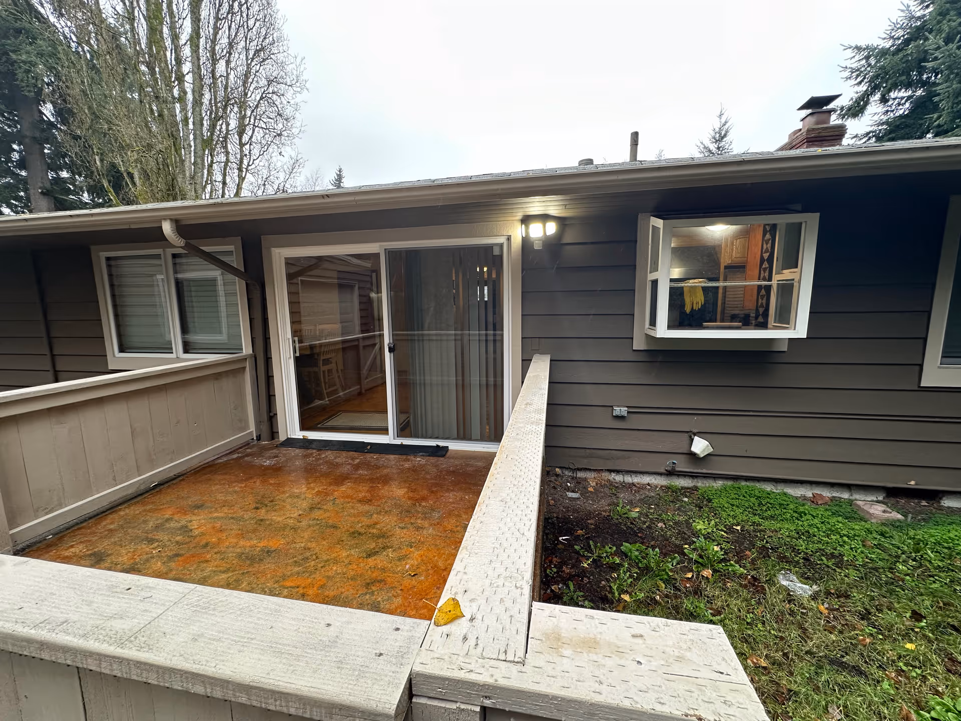 Back wooden deck with sliding glass door, railing, and dark exterior siding of a single-story home.