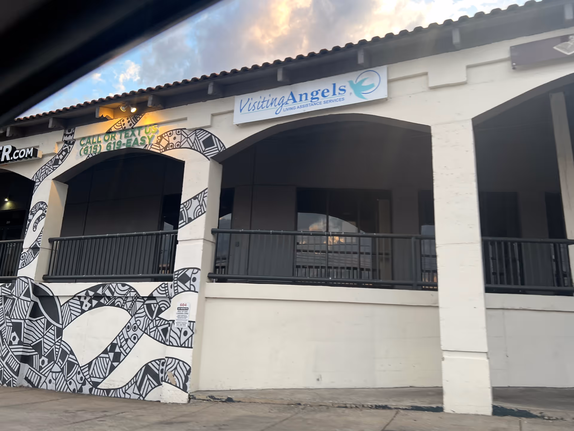Exterior view of Visiting Angels building with arched entrance, mural, and balcony.