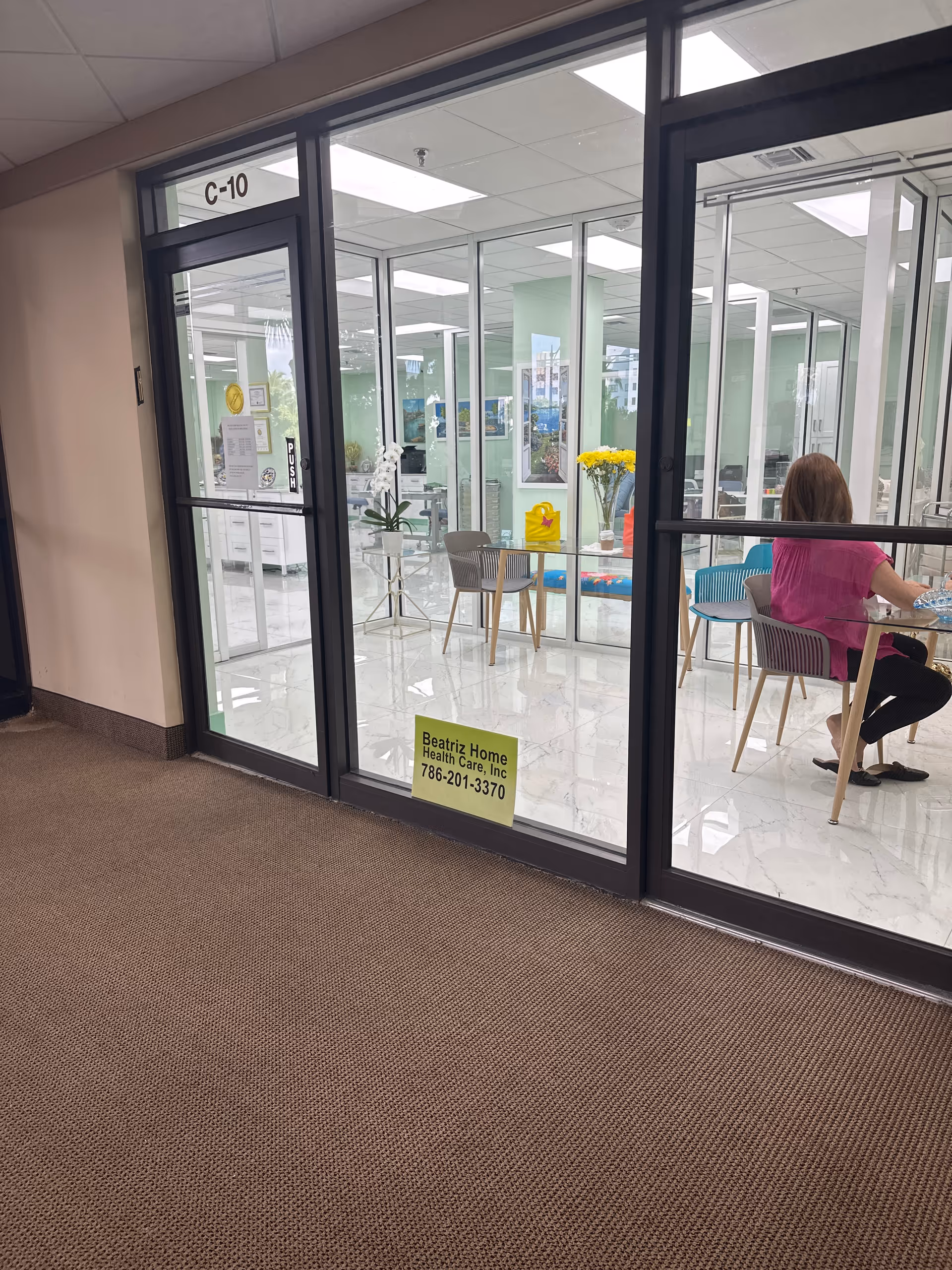 Glass-walled reception area inside Beatriz Home Health Care with a woman seated at a table.