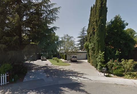 Exterior driveway to a facility entrance with parked cars and tall trees.