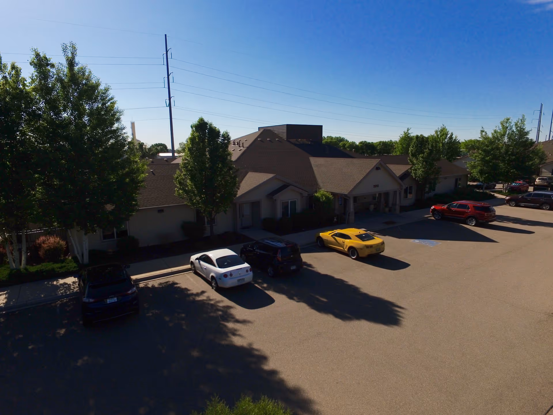Exterior front of a one-story senior living building with trees and a parking lot containing several cars.