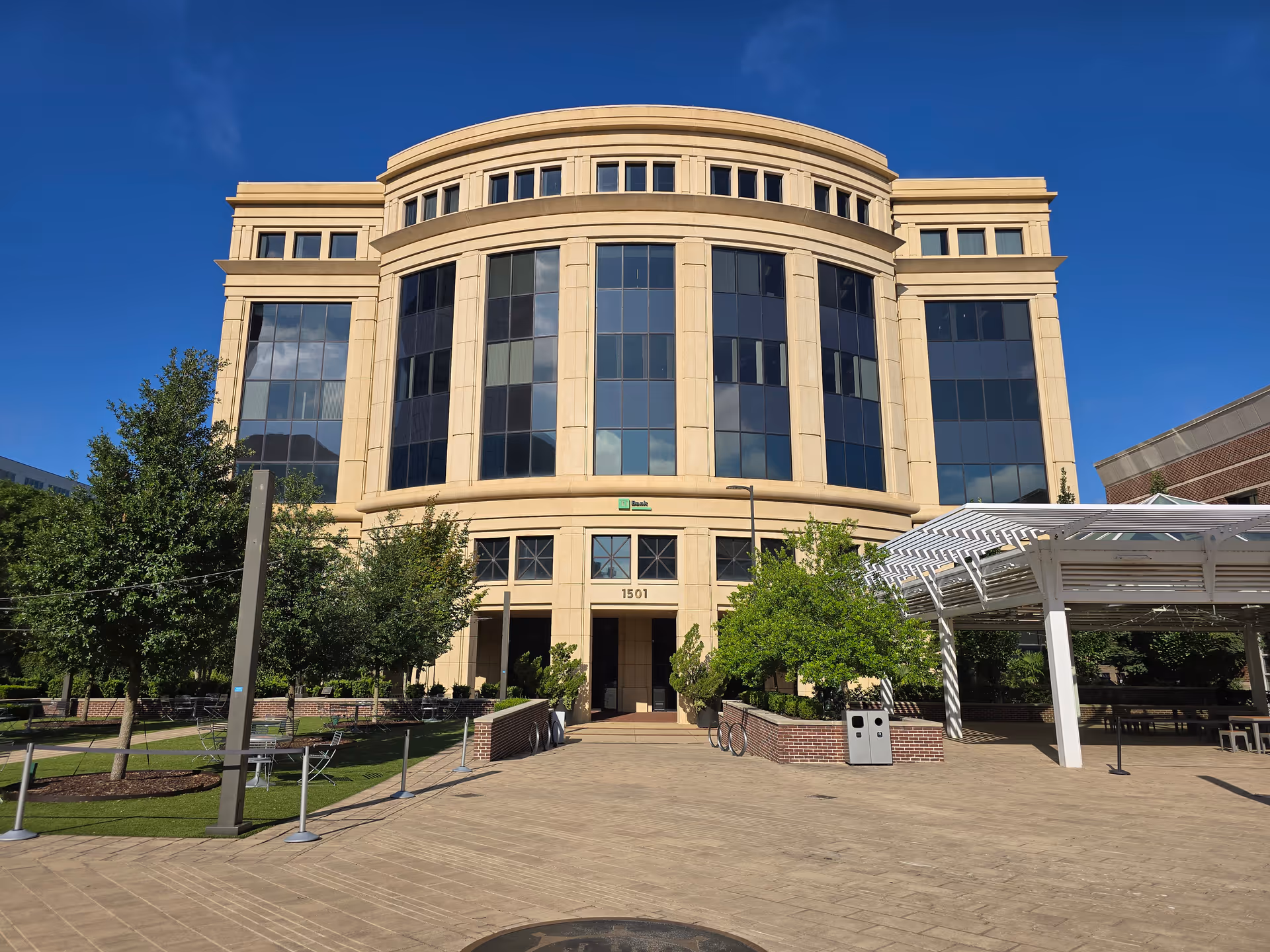 Large beige building with curved glass facade and trees in front.