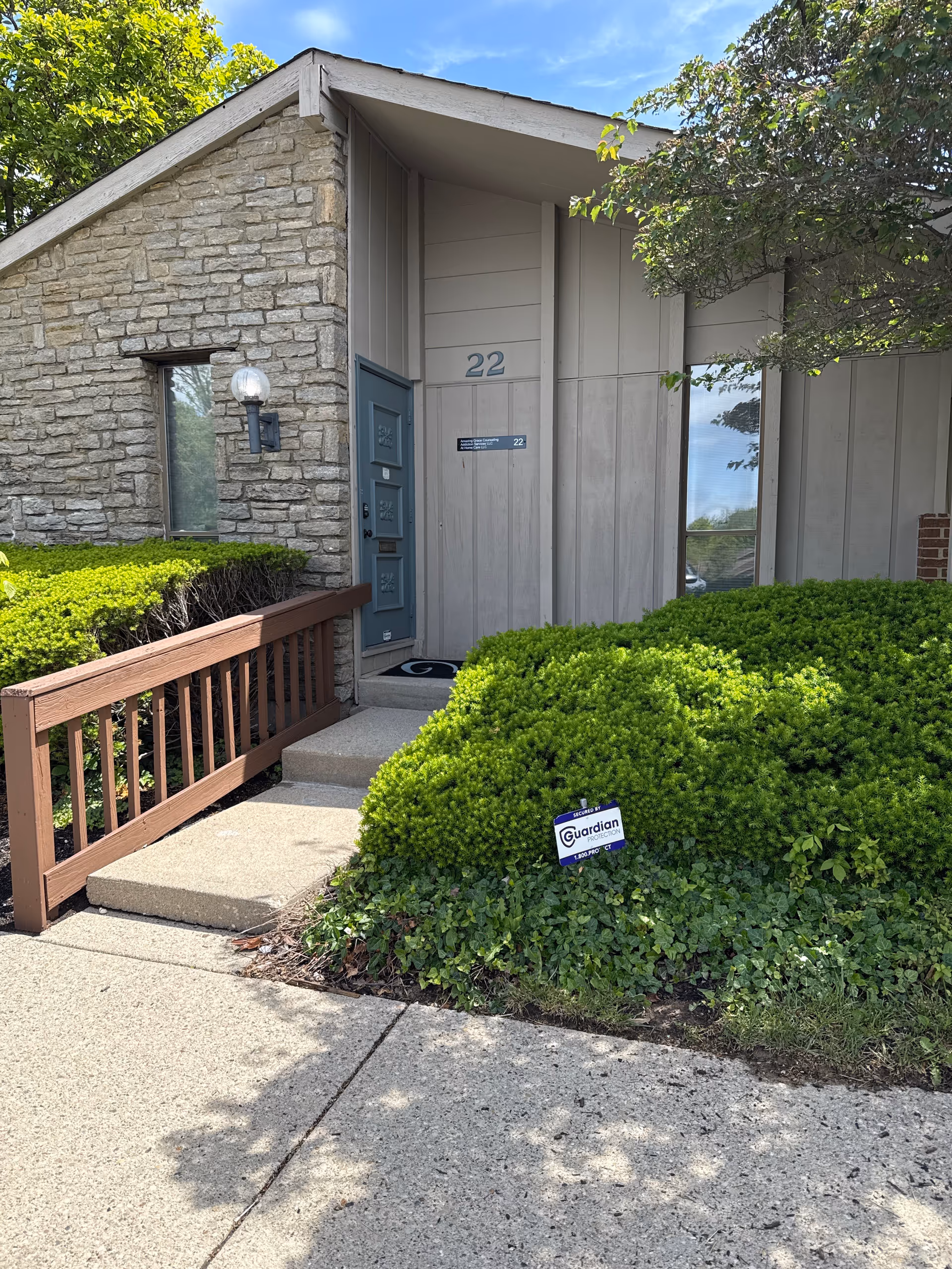 Front entrance of a senior living facility with stone wall, door, and green shrubs.