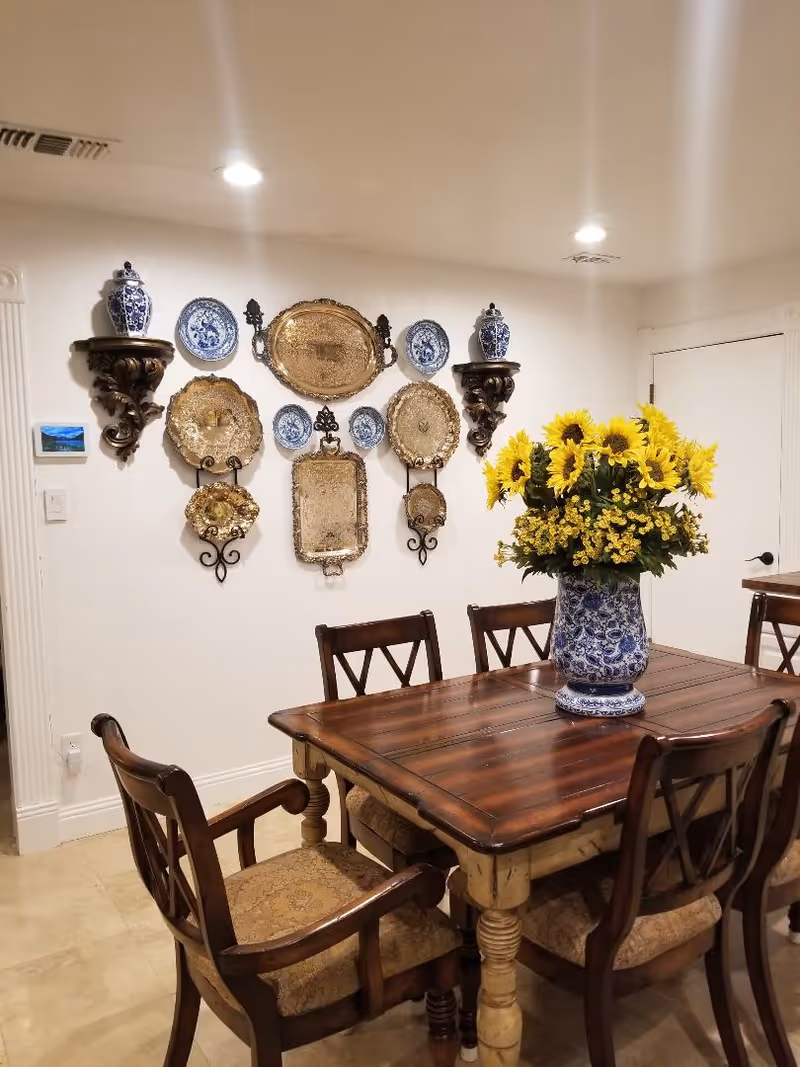 A wooden dining table with chairs and a blue-and-white vase of sunflowers in a dining room.