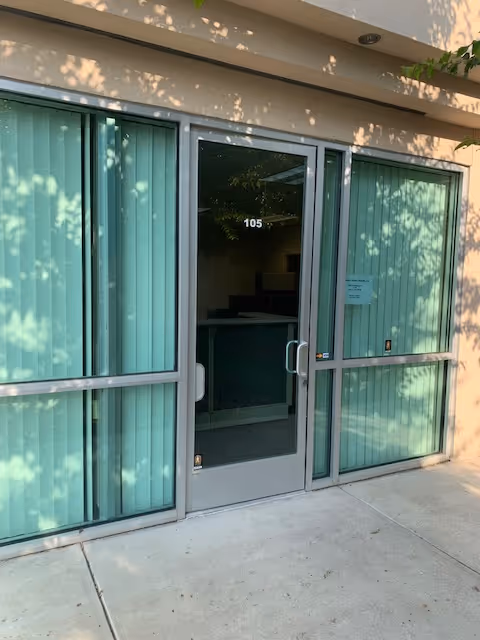 Glass front entrance with green blinds and a door labeled 105, outside concrete walkway.