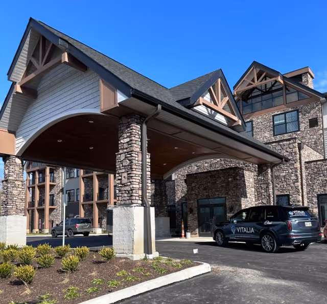 Stone-faced senior living facility entrance with a covered porte-cochère and a Vitalia van.