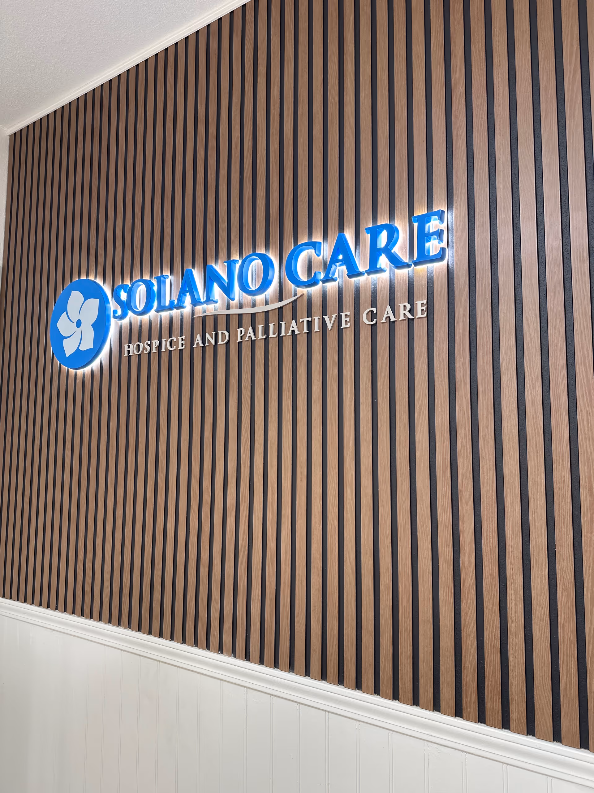 Interior wall with vertical wood slats and illuminated Solano Care sign.