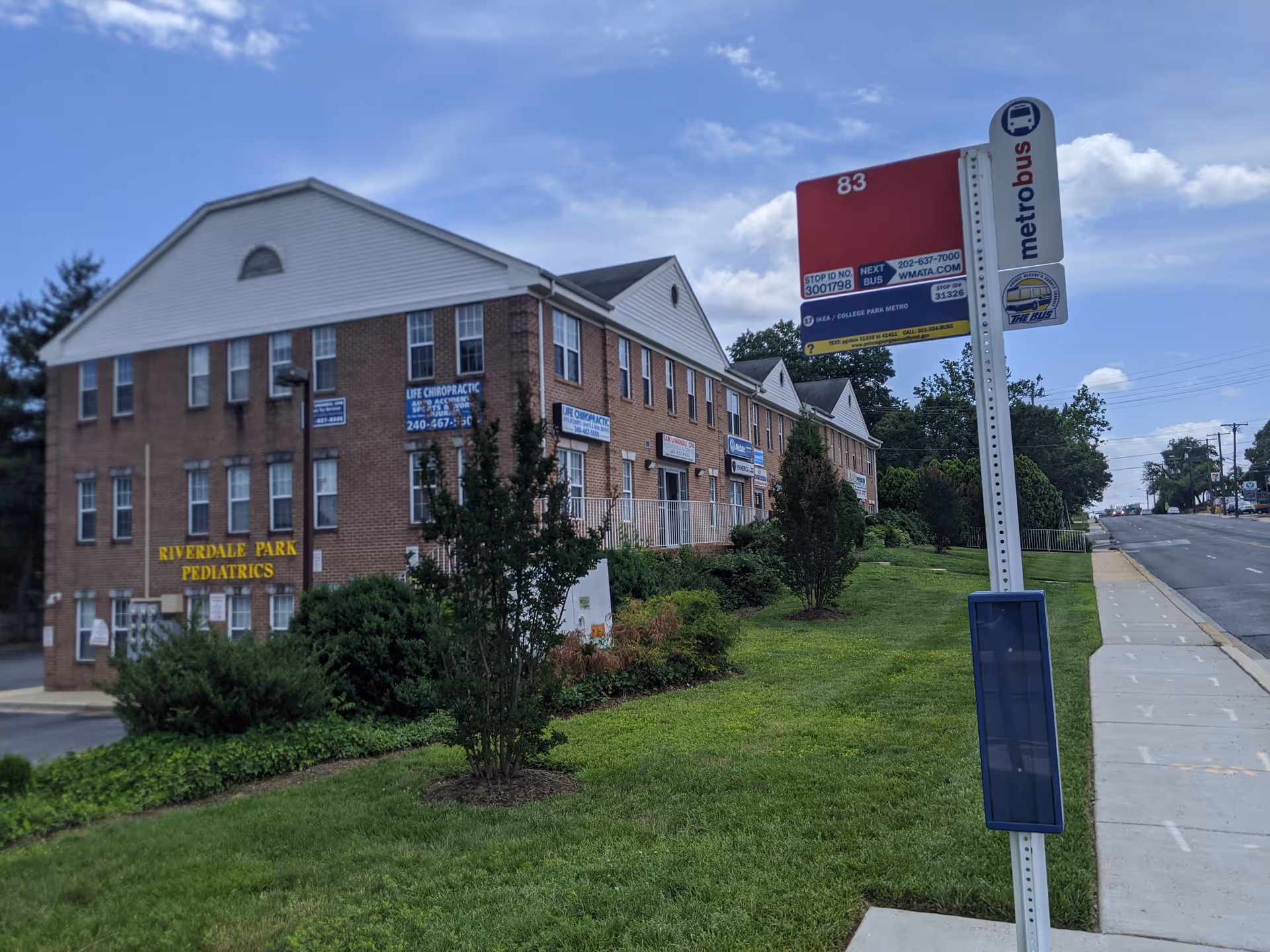 Brick building with multiple windows and a bus stop sign along the street
