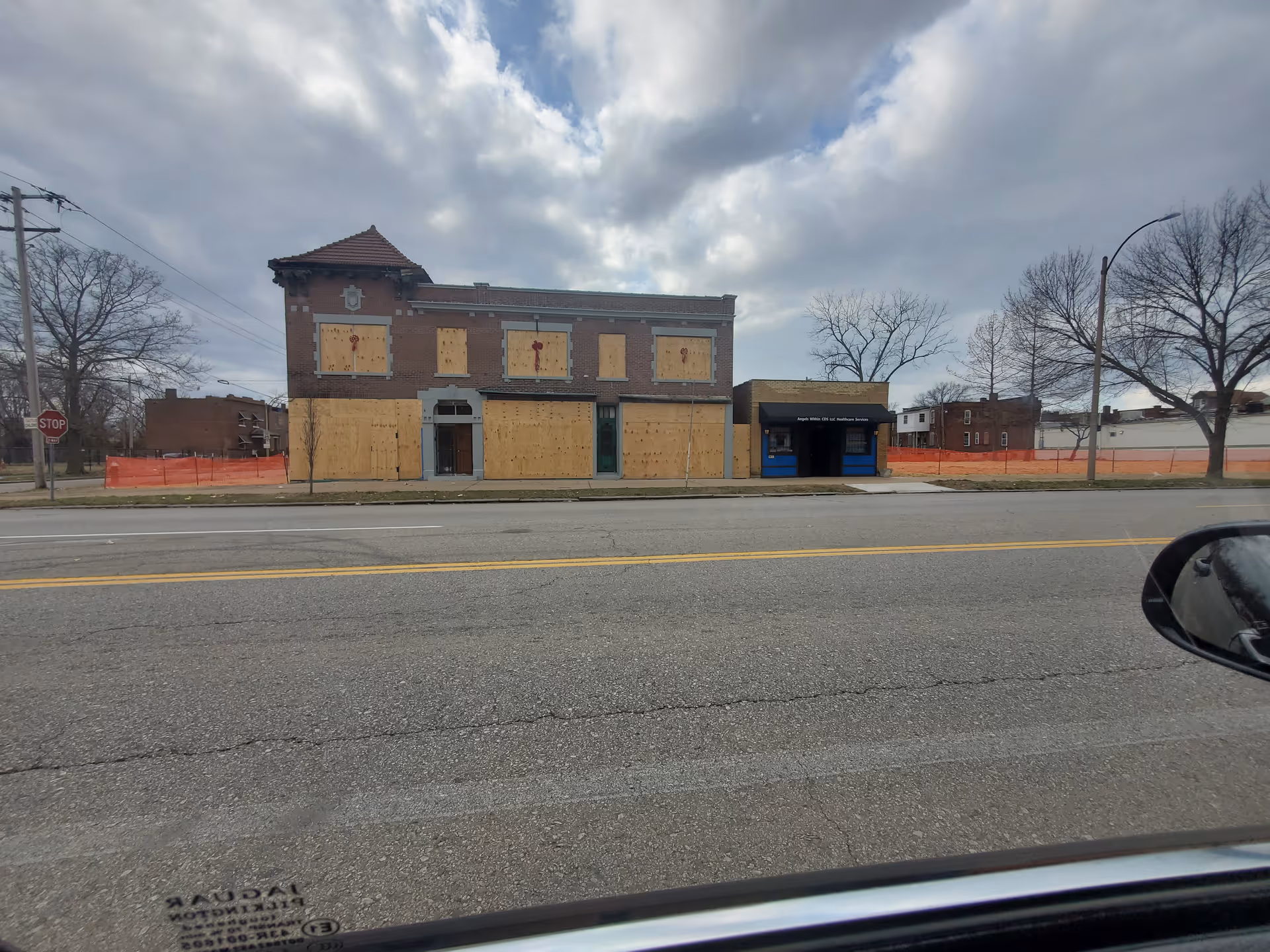 Boarded-up brick building along a street with orange fencing and a blue storefront.