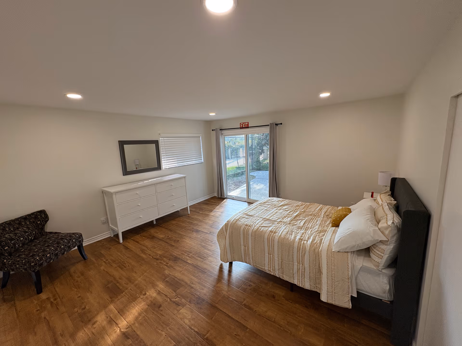 A spacious bedroom with a bed, dresser, chair, and sliding glass door to outside.