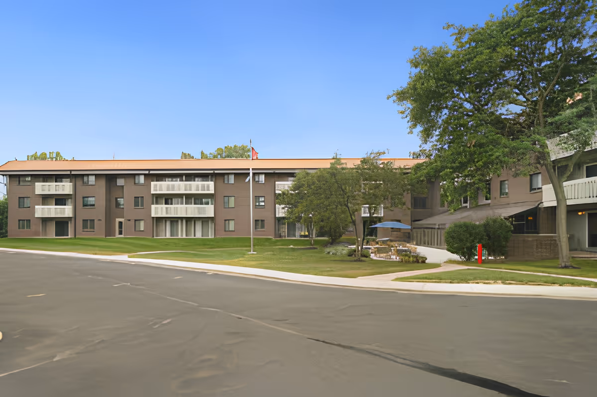 Exterior view of King's Reserve College Park, showing a multi-story building with balconies, a flagpole, green lawn, trees, and a paved driveway under a clear blue sky.