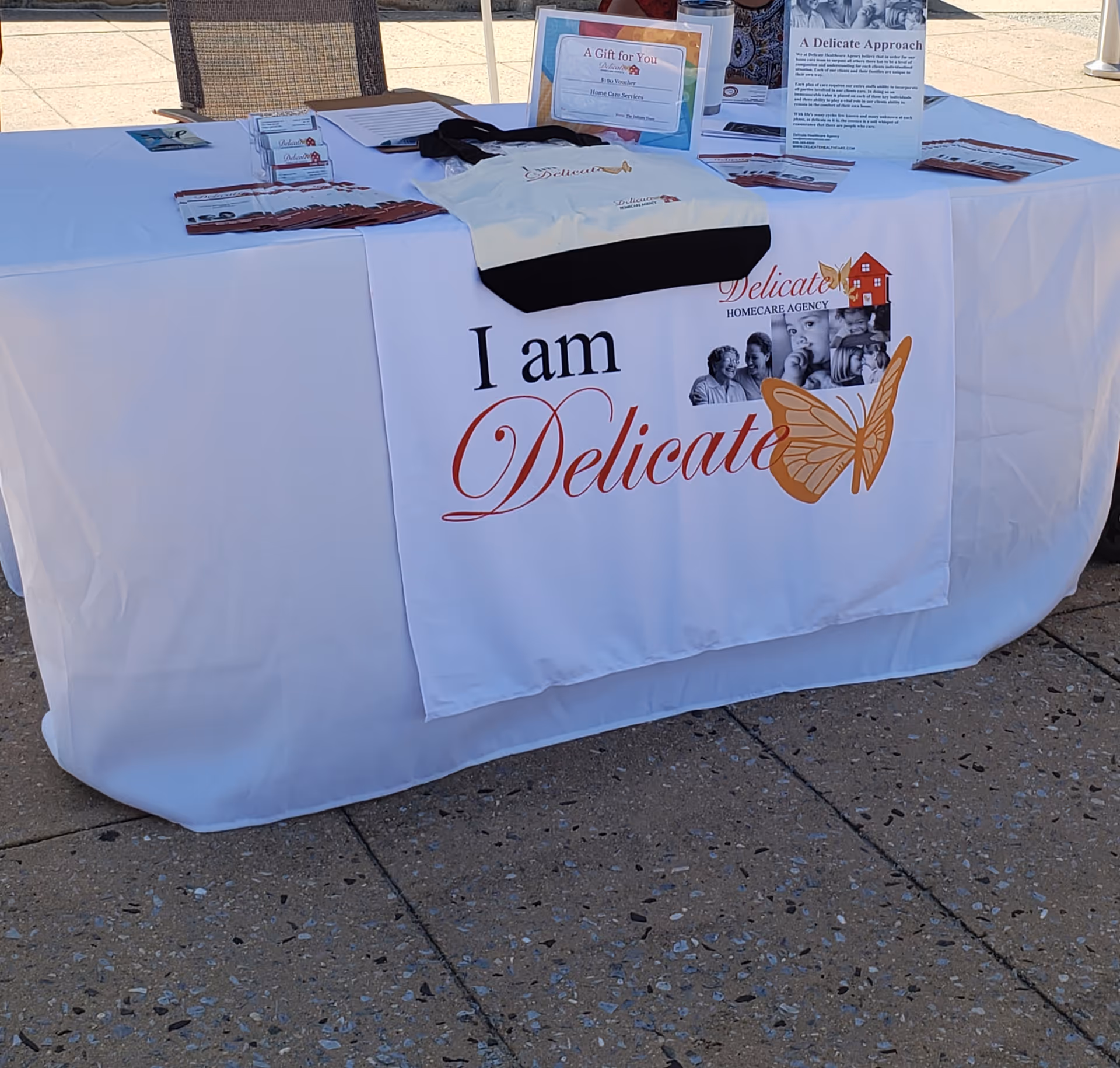 Outdoor event table with brochures and a Delicate Homecare banner on a white tablecloth.