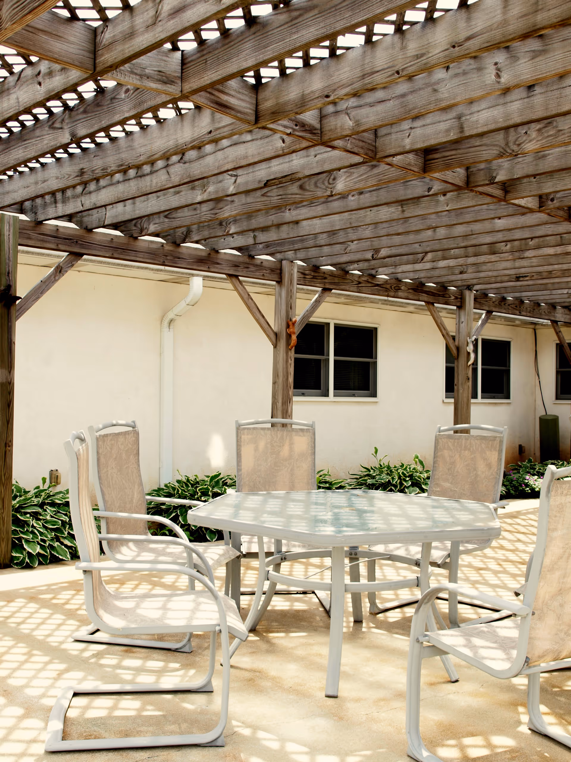Outdoor patio with a white round table and multiple beige chairs under a wooden pergola.