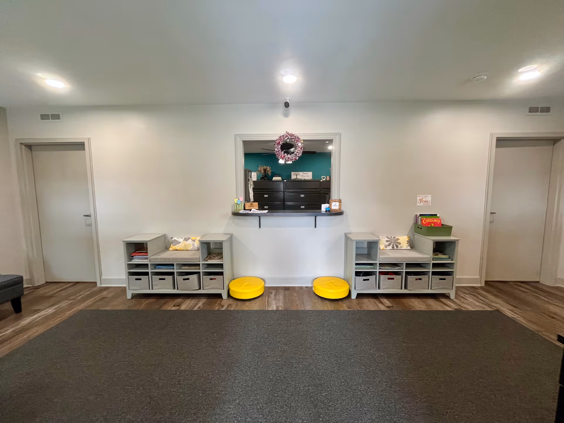 Reception window with teal back wall, cubby shelves, and two yellow stools.