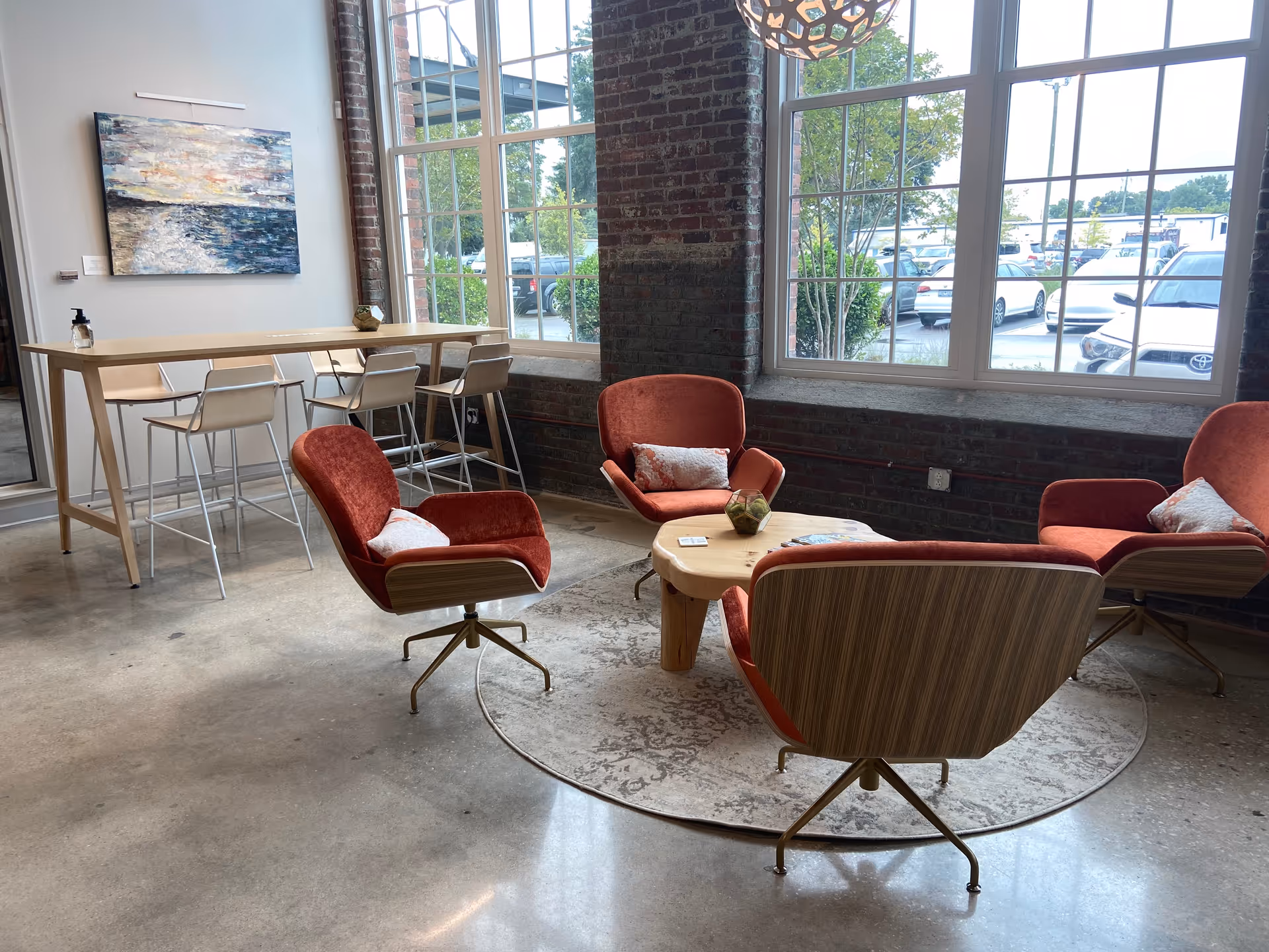 Modern lounge in a senior living facility with red chairs, a coffee table, and large windows.