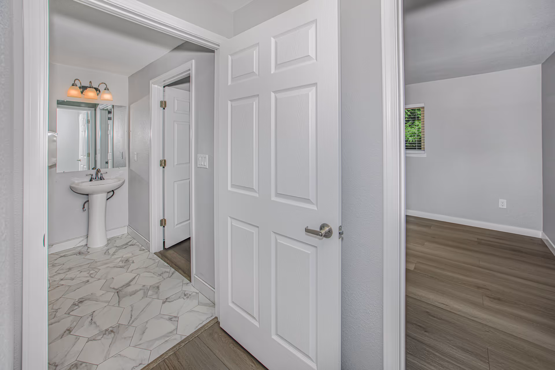 Bathroom with pedestal sink, mirror, and marble floor; doorway opens to hall and room.