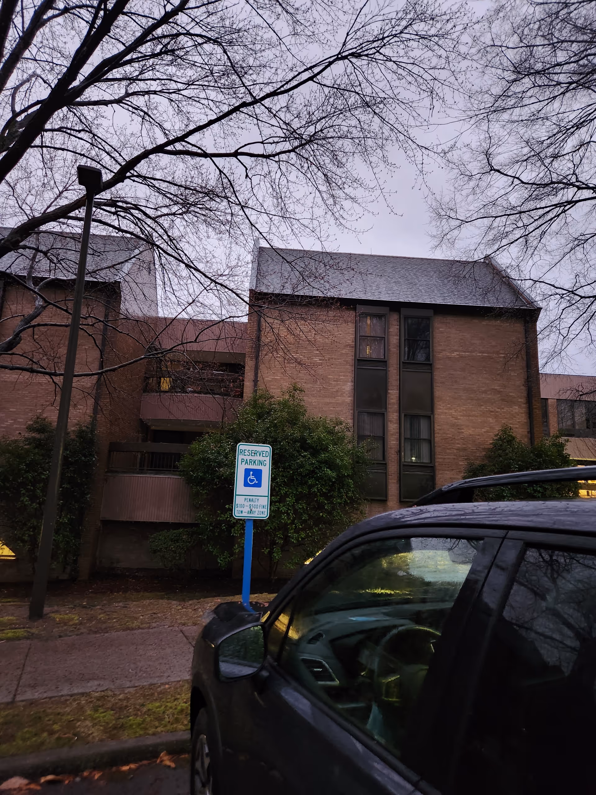 Exterior view of a brick senior living building with trees and a handicap parking sign.