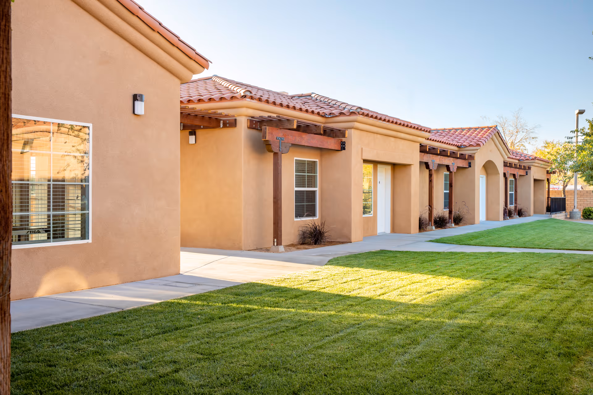 Exterior view of a tan, tile-roofed senior living building with a green lawn.