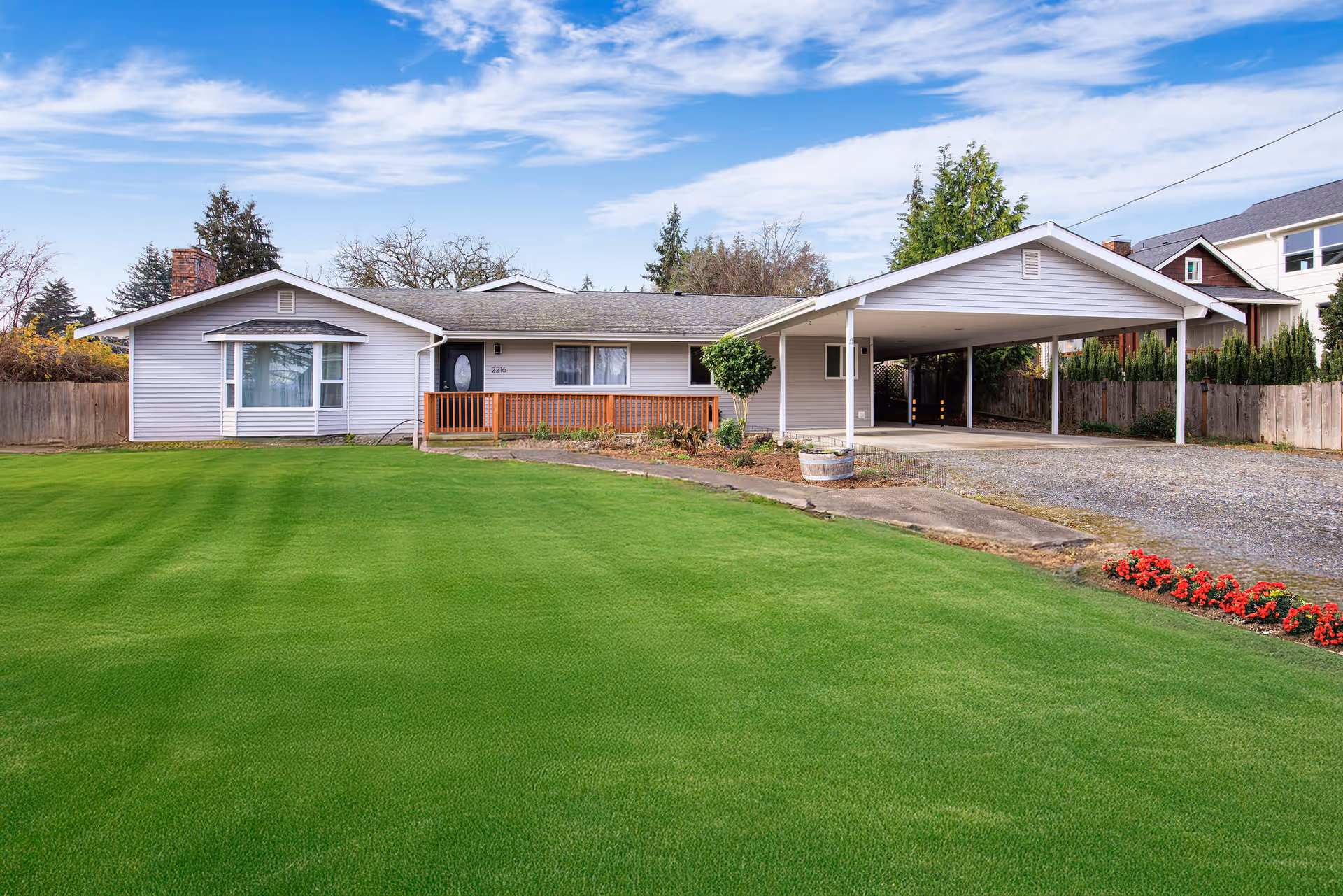 Single-story house with green lawn, gravel driveway, and front carport.