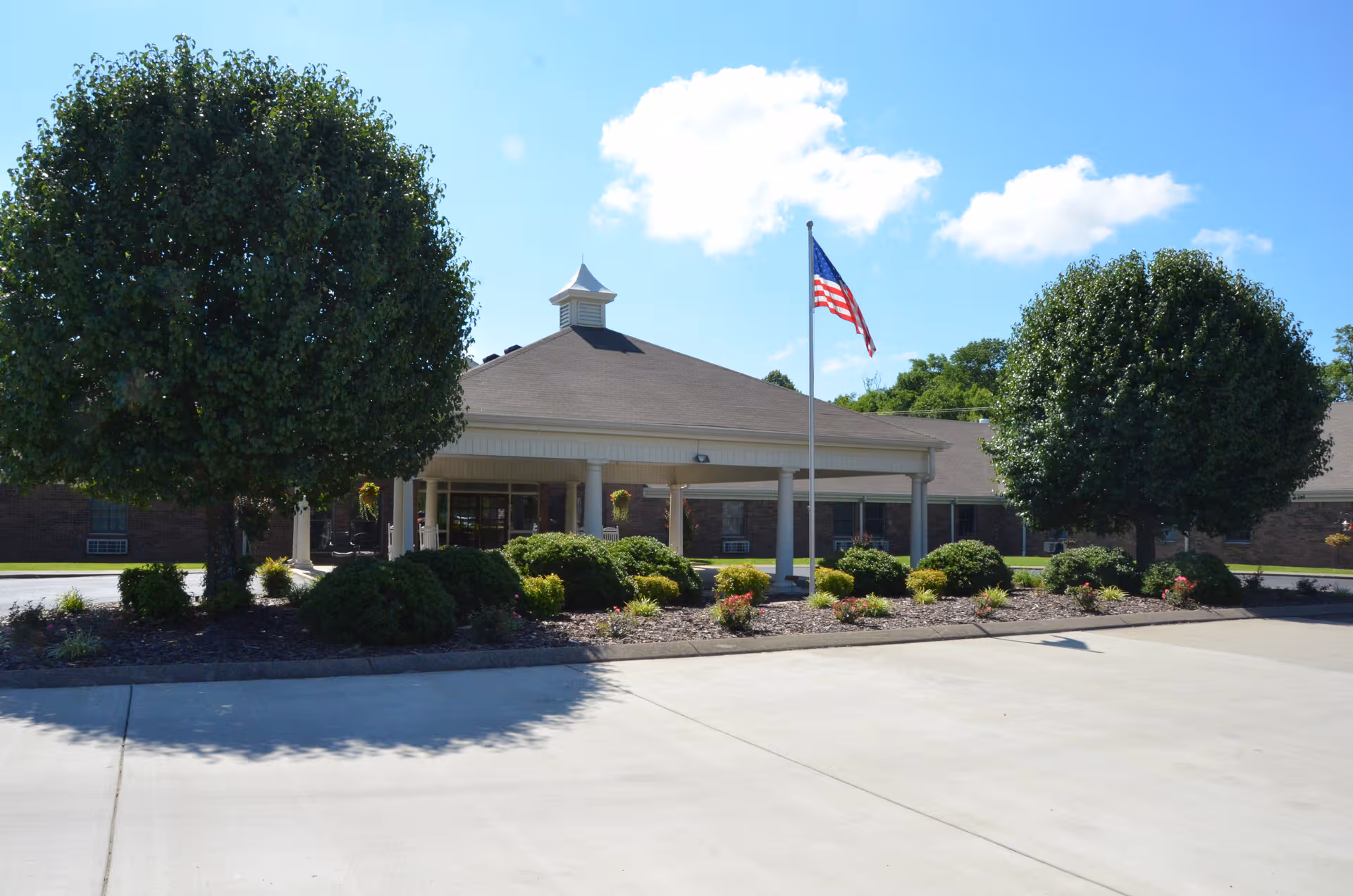 Exterior view of Village Manor Assisted Living entrance with landscaping and flag