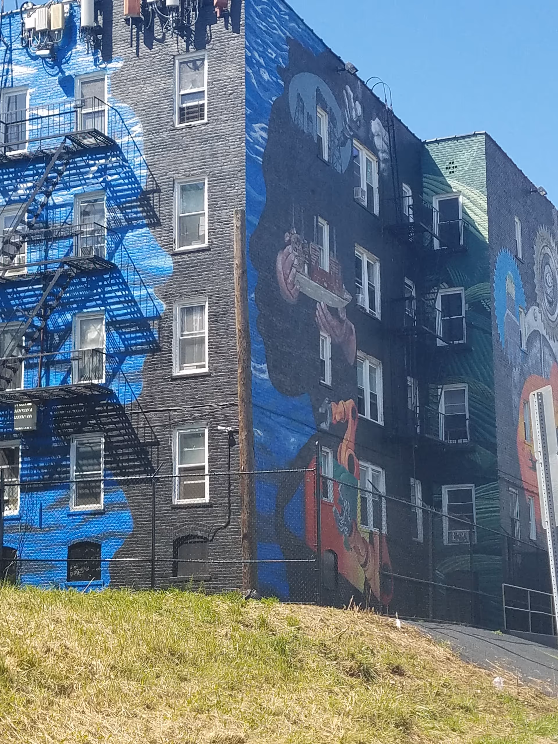 Exterior view of a brick building with a colorful mural and a metal fire escape.