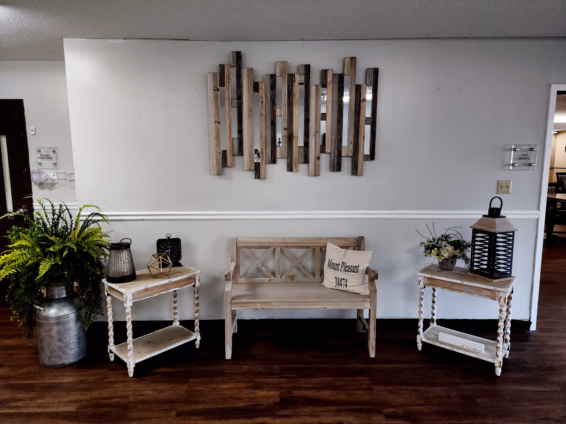 A rustic lobby area with a wooden bench, two matching side tables, plants, and wall art.