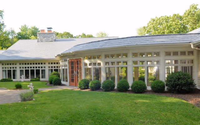 Exterior of a senior living facility with a glass-front entrance and trimmed shrubs.