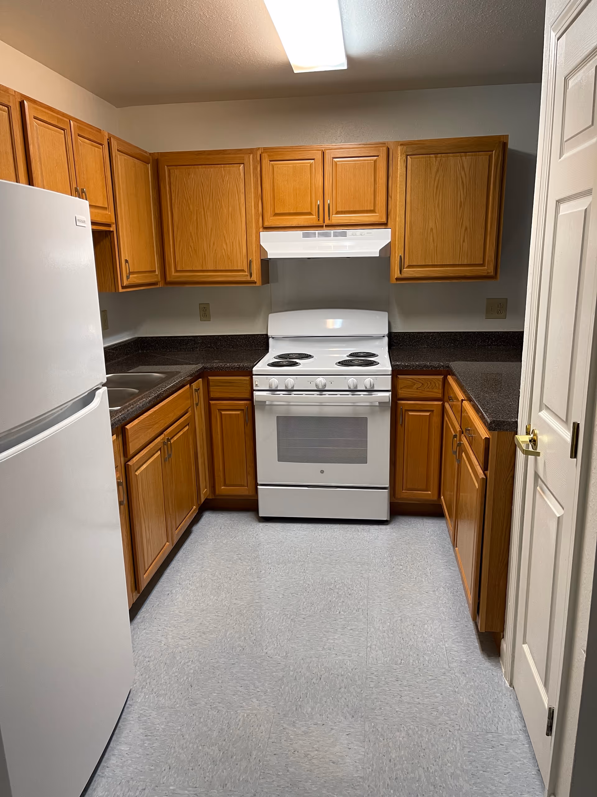Compact kitchen with wooden cabinets, white stove, and refrigerator in a senior housing unit.