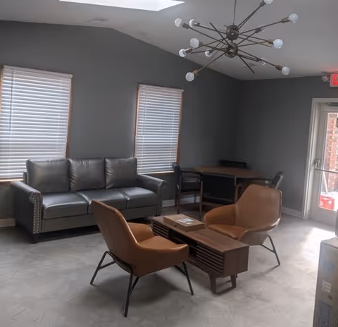A modern living lounge with a gray sofa, chairs, tables, and a chandelier.