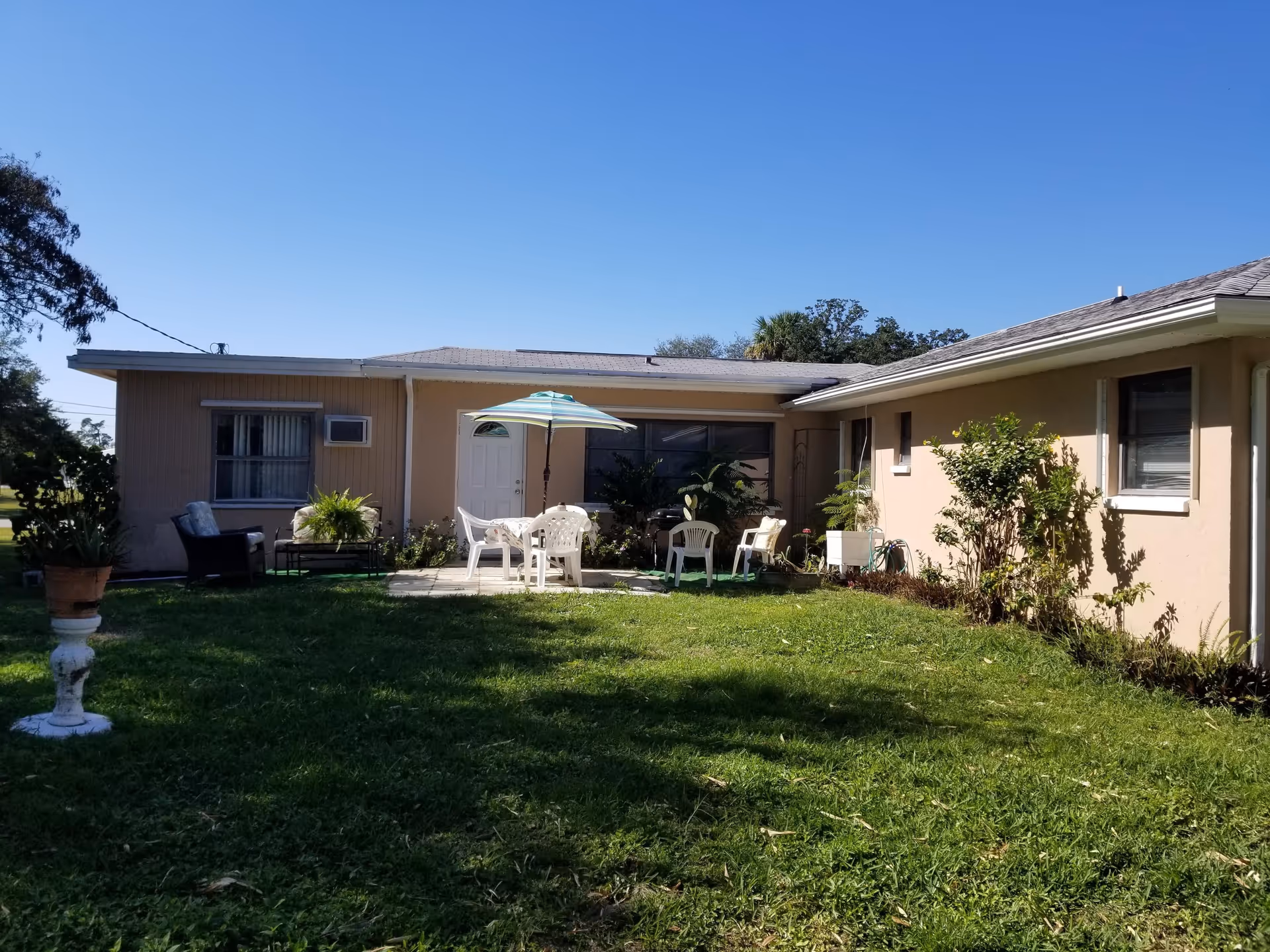 A single-story beige facility with grassy yard and outdoor seating under an umbrella.