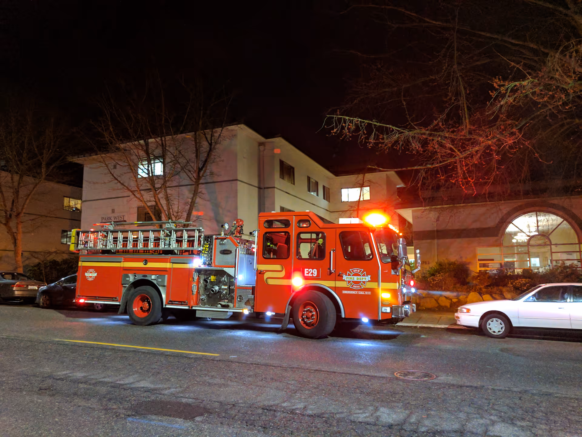 Nighttime exterior view of a red fire truck parked in front of a senior living facility.