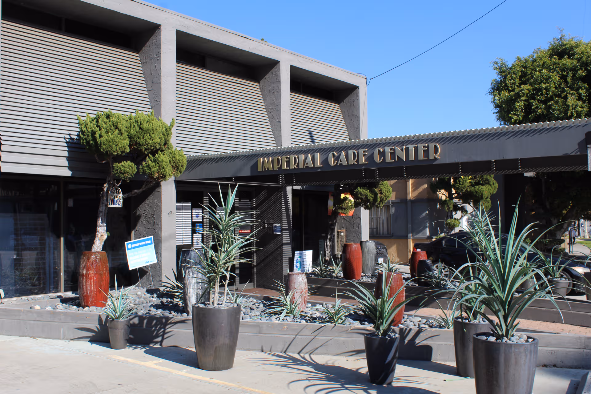 Exterior view of Imperial Care Center entrance with potted plants and blue sky.