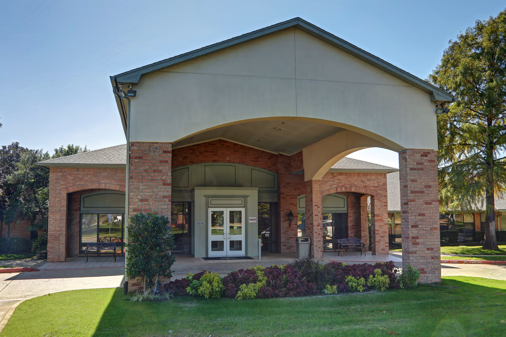 Front entrance of Parkwood Healthcare facility with brick pillars, arches, and landscaped courtyard.