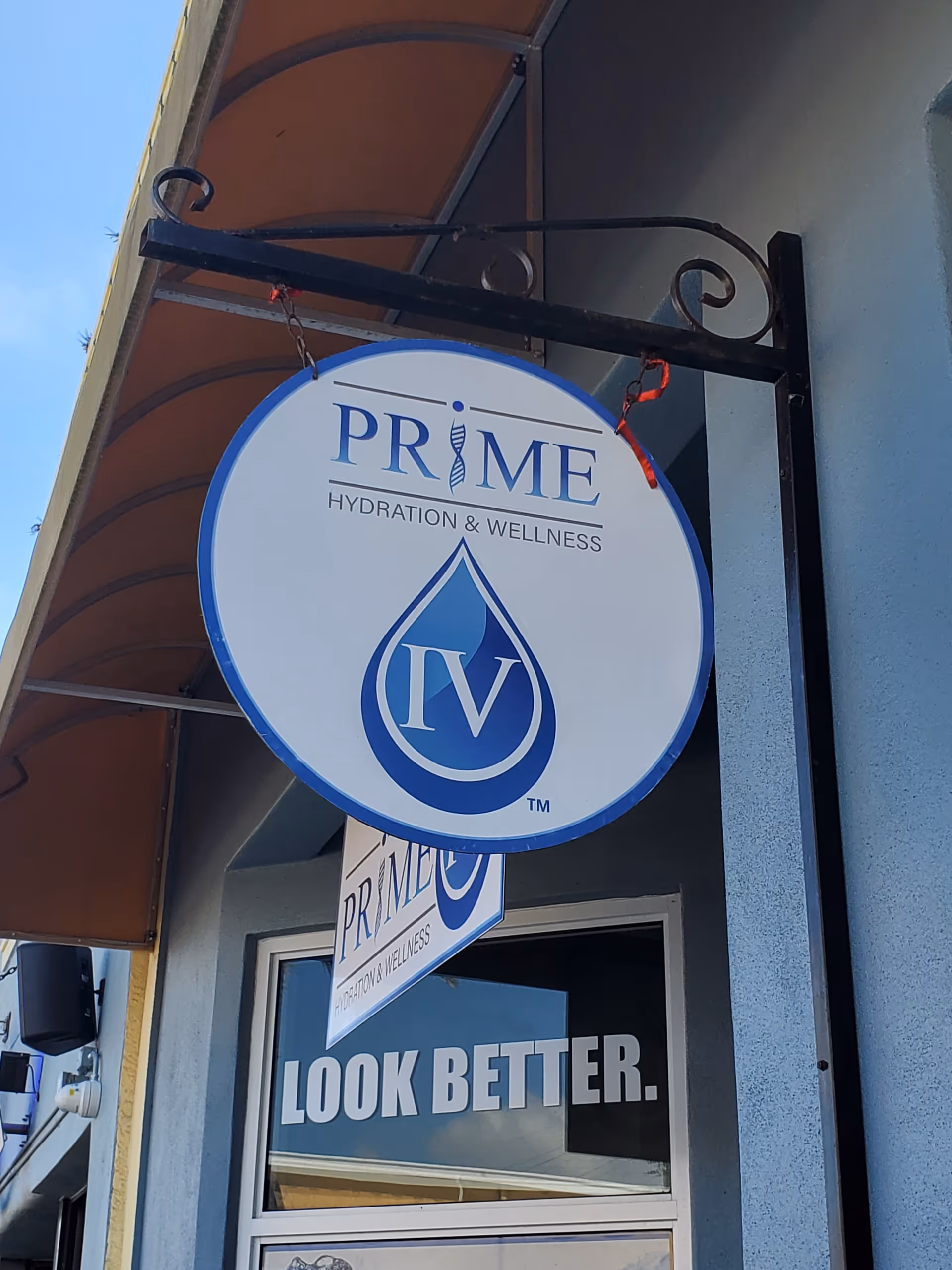 Large round Prime IV Hydration & Wellness sign hanging on a building exterior.