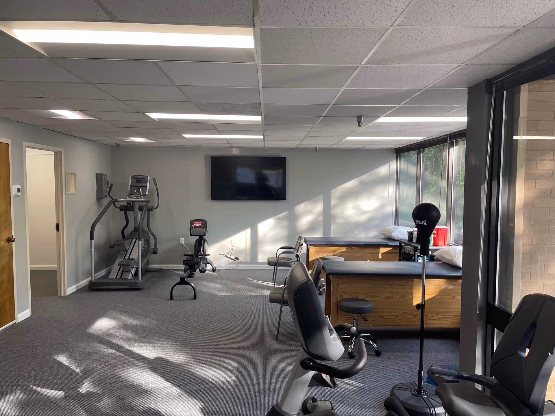 A rehab gym in a senior facility featuring treadmills, a stationary bike, and treatment tables.