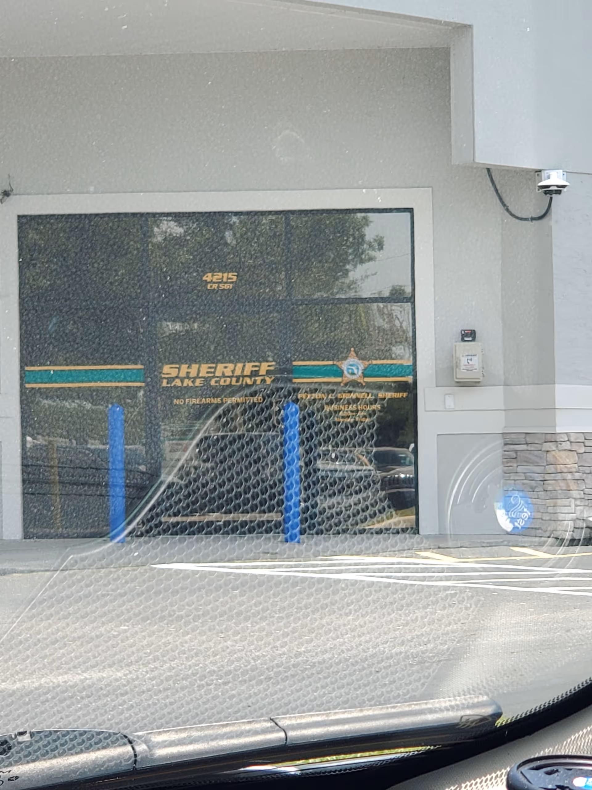 Sheriff vehicle labeled Lake County sits behind a chain-link fence at a building entrance.