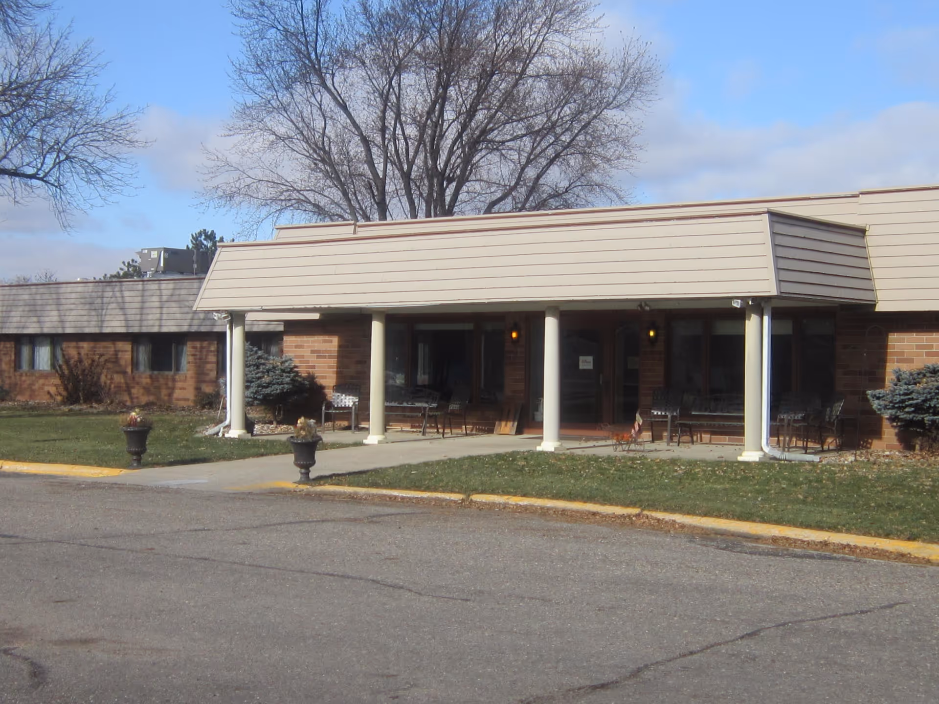 Exterior view of a brick senior living facility with a covered entrance and outdoor seating.