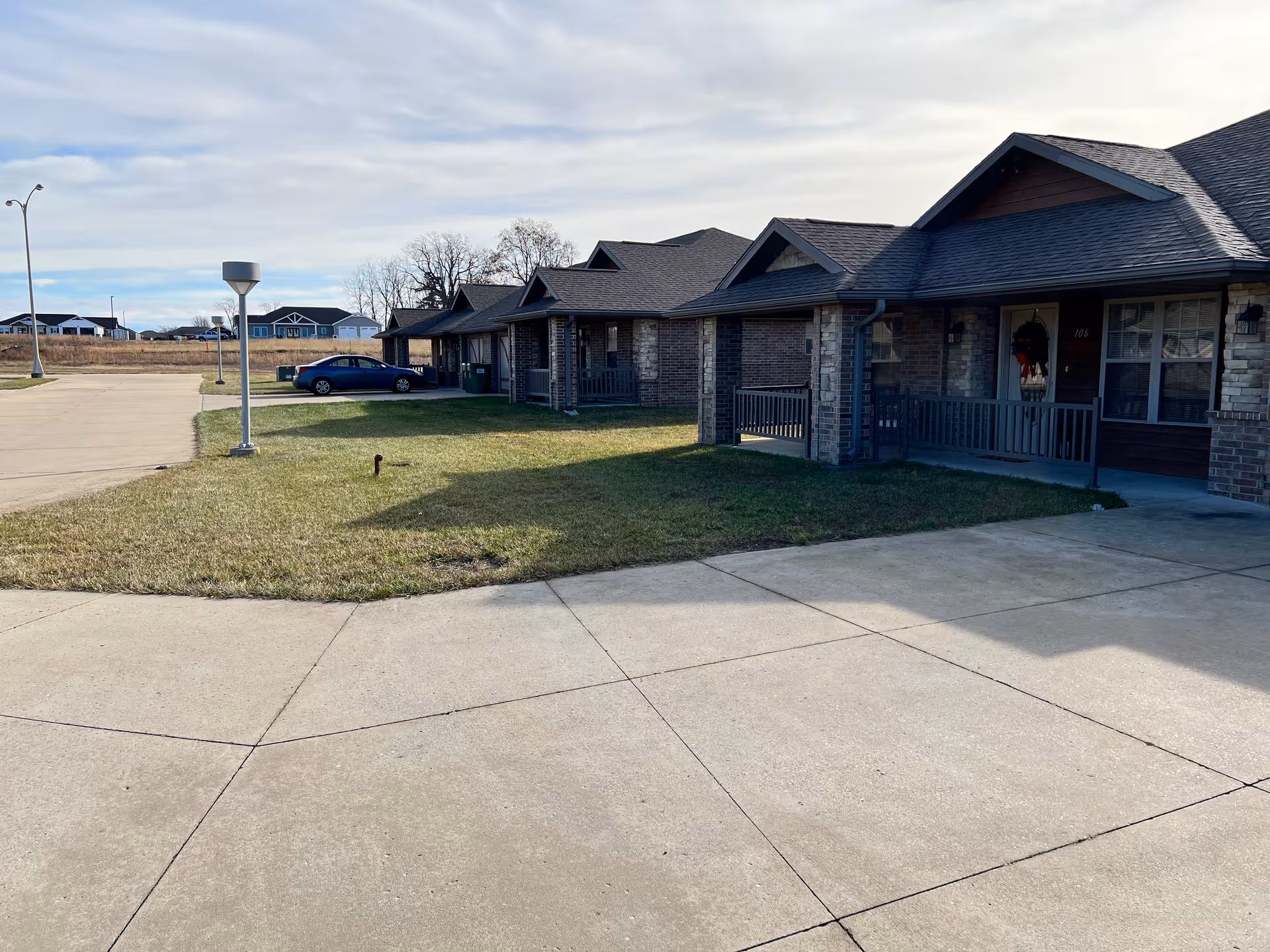Row of brick senior living cottages with porches and a paved parking area.