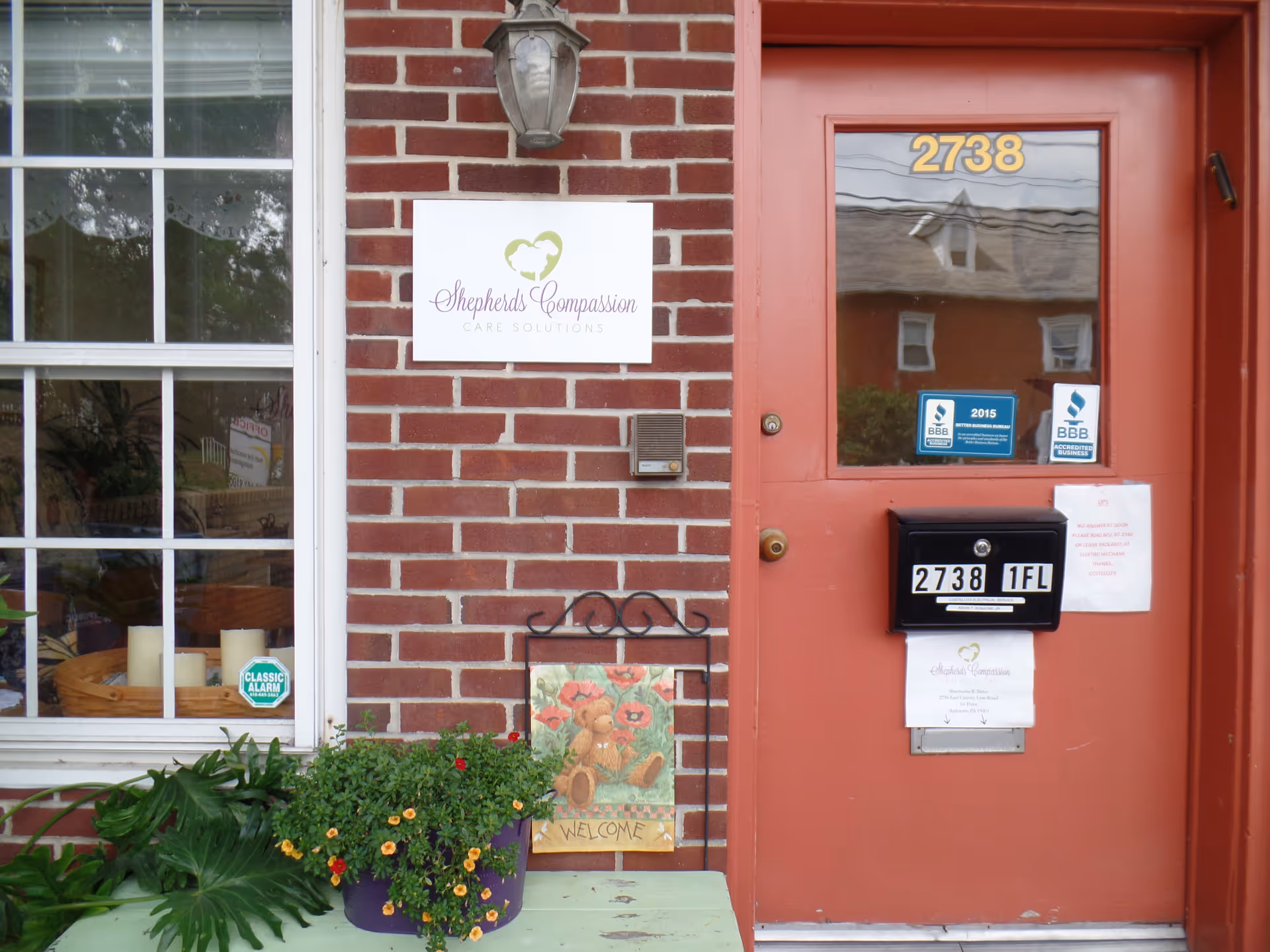 Brick building exterior with a red door and a sign for Shepherds Compassion Care Solutions.