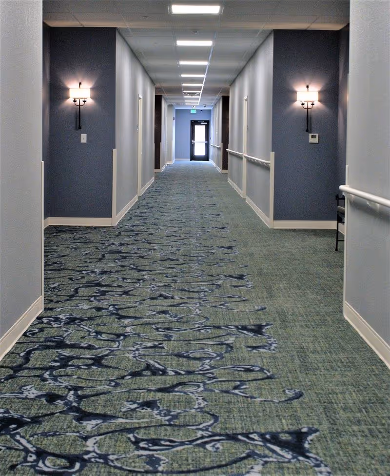 Long interior hallway inside Kinwell at South Lyon with blue walls and sconces.