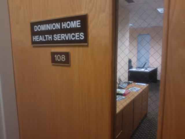 Wooden door with Dominion Home Health Services sign; office desk visible inside.