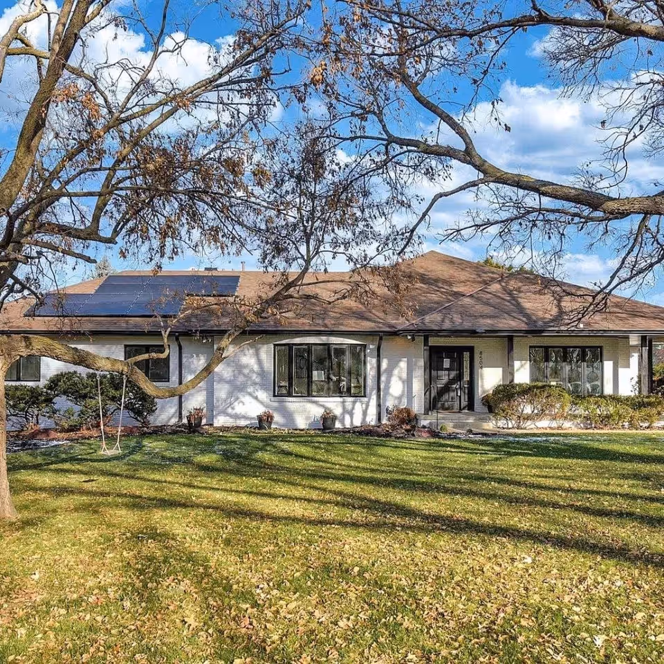 Single-story building with solar panels, front yard, and leafless tree branches.
