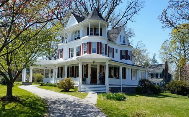 White Beechwood Assisted Living exterior: Victorian-style house with wraparound porch and lawn.