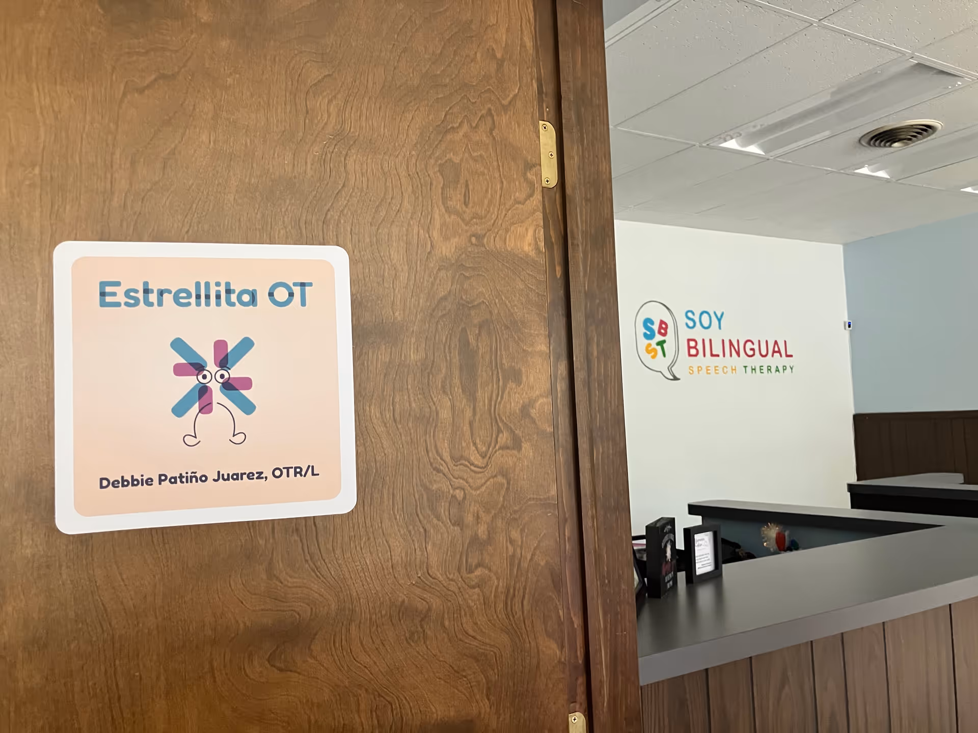 Wooden door opens to a reception area with Estrellita OT sign and bilingual speech therapy sign.