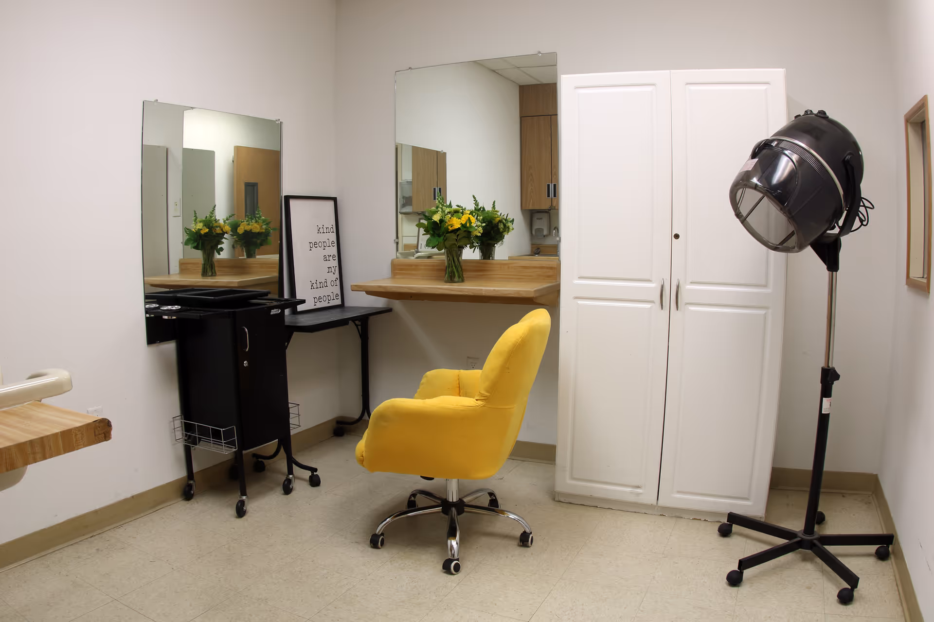 Interior view of a salon area with a yellow chair, mirrors, white cabinet, and hair dryer.