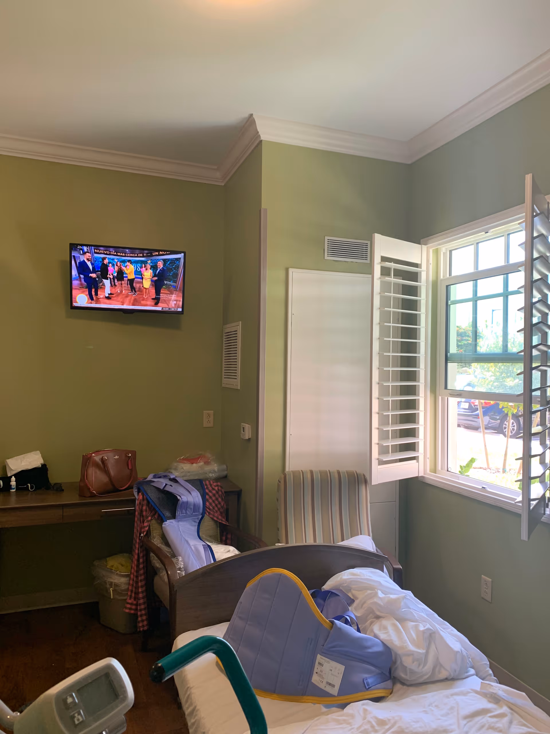 A patient room with a bed, a chair, a walker, window, and TV.