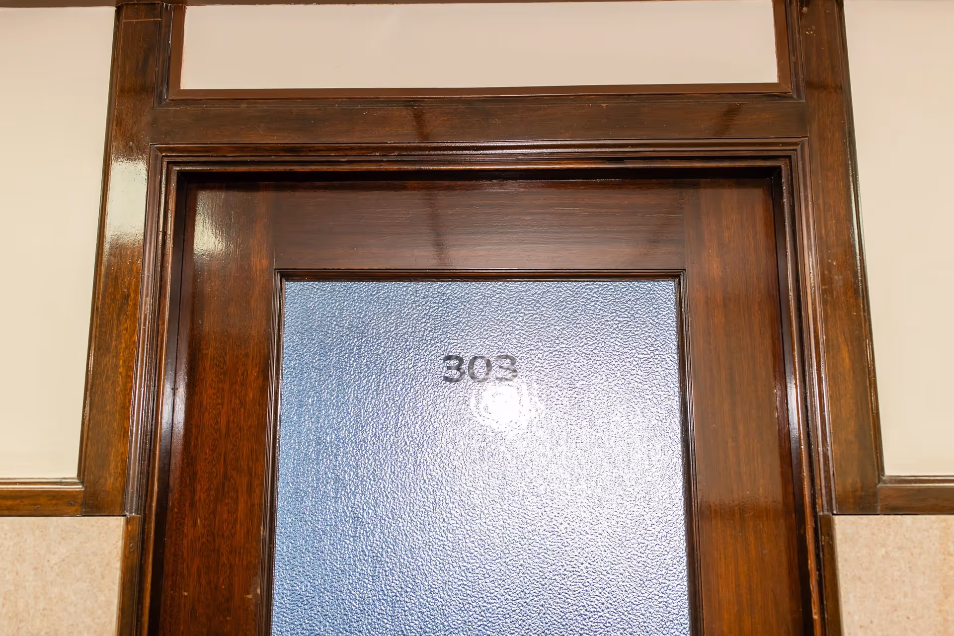 A blue numbered door 303 framed by dark wood in an interior hallway.