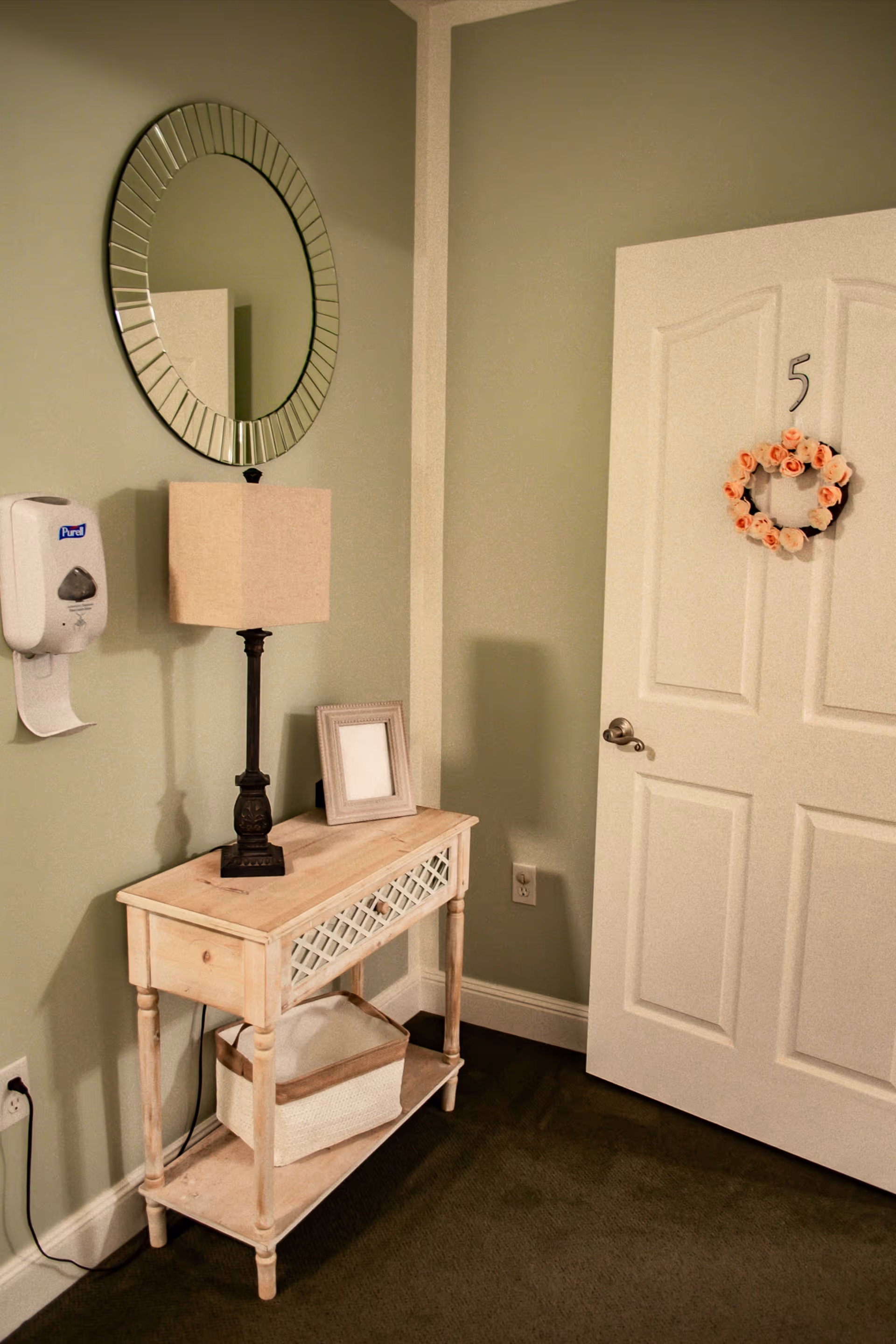 Entryway with a small wooden console table, lamp, mirror, wreath on door, and tidy decor.